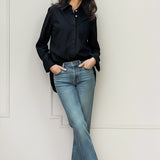Woman wearing a black shirt by Room502 and blue jeans against a white wall