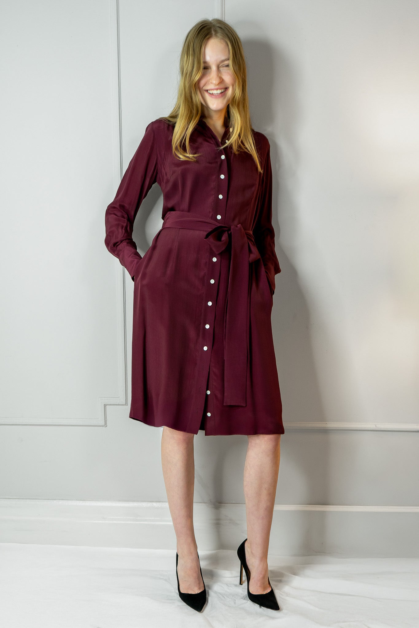 Woman wearing a burgundy dress with a belt against a white wall - dress by Room502