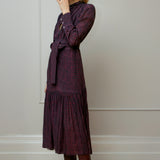 Woman wearing a dark purple print dress with a pattern, standing against a plain wall - by Room 502