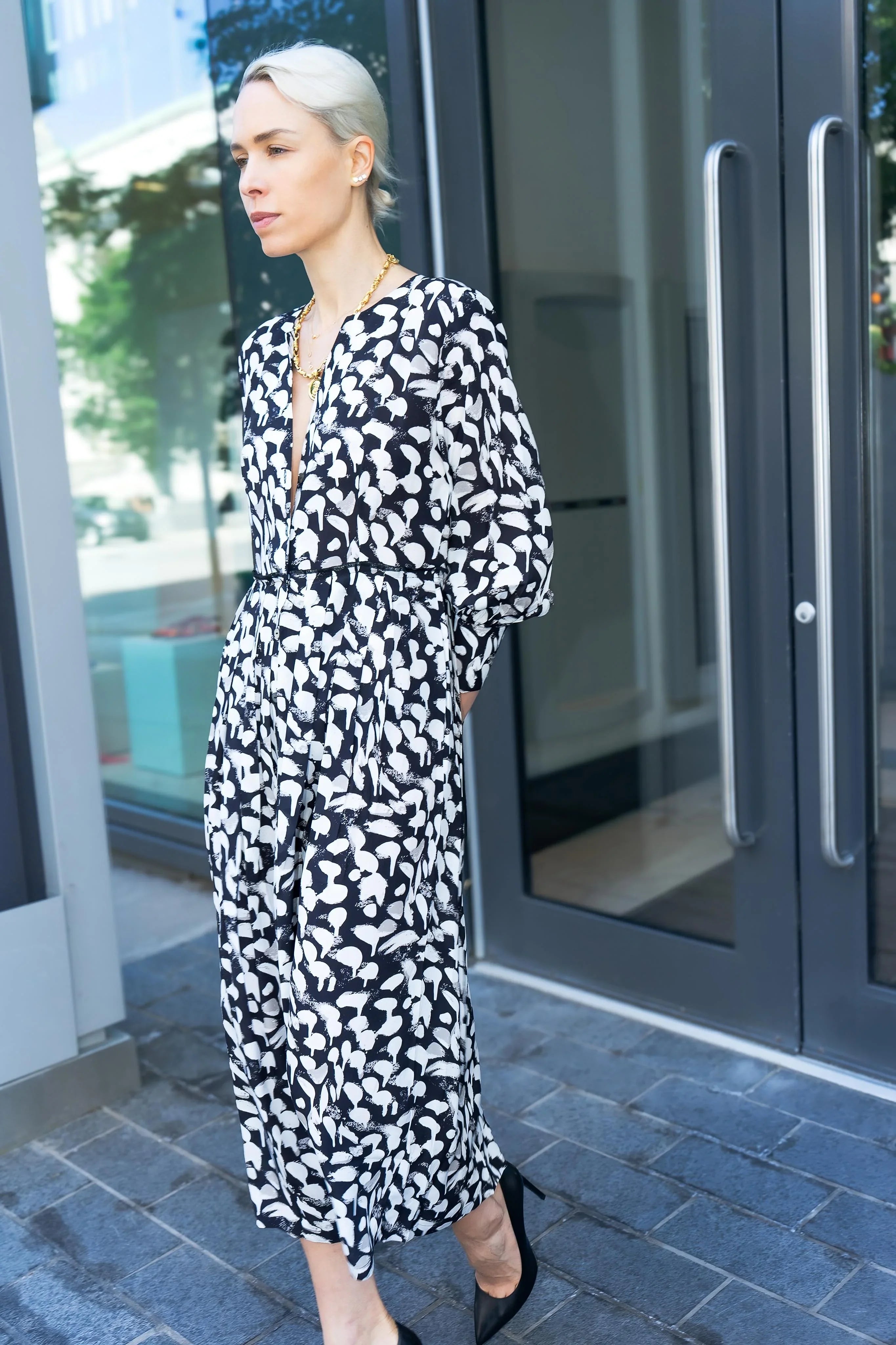 Woman in a black and white patterned dress standing outside a building.