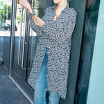 Woman in a patterned caftan and jeans standing outside a building.