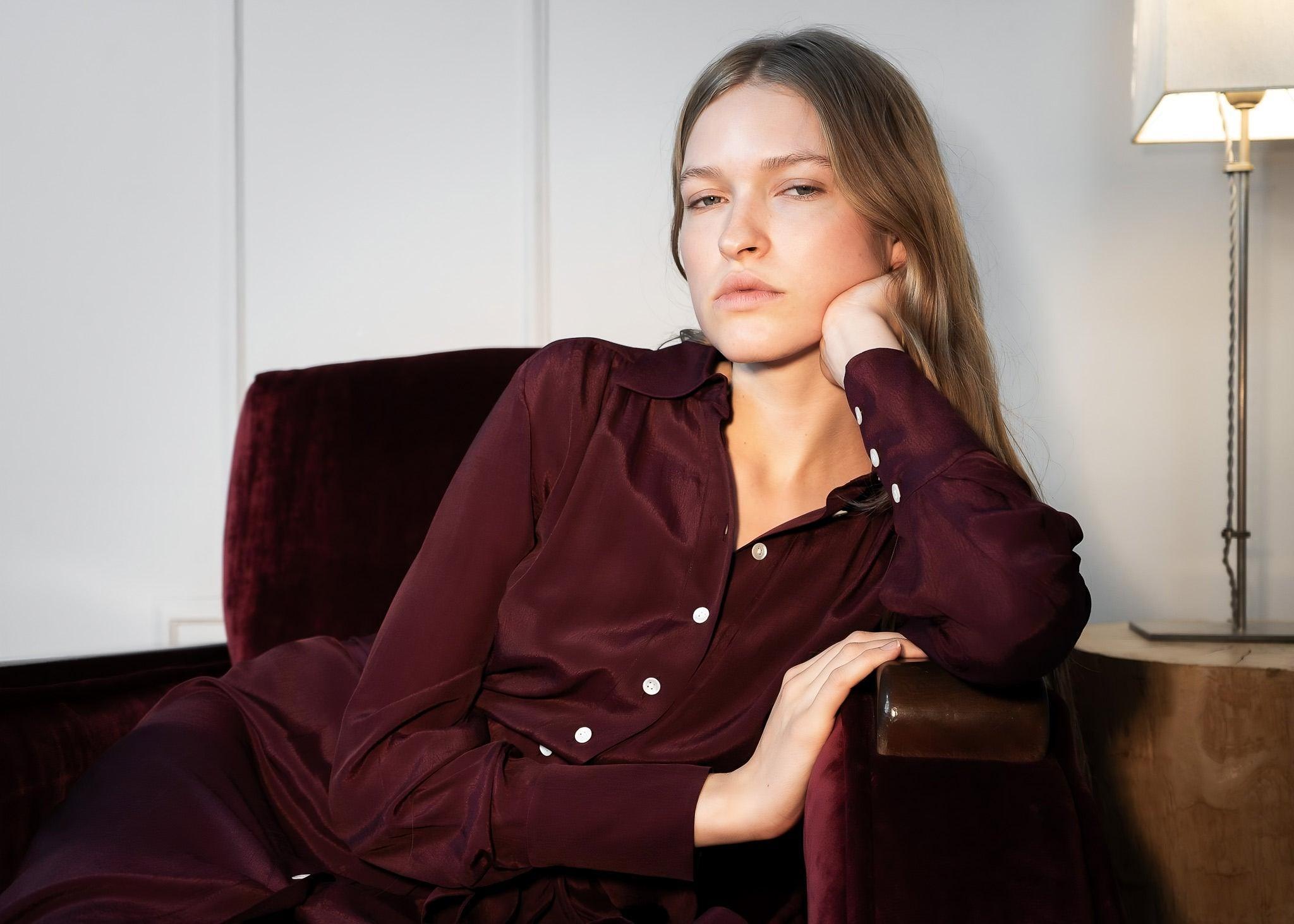 Woman in burgundy dress sitting in a chair indoors.