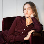 Woman in burgundy dress sitting in a chair indoors.