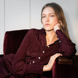 Woman in burgundy dress sitting in a chair indoors.