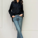 Woman wearing a black shirt by Room502 and blue jeans against a white wall