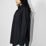 Person wearing a black oversized shirt and light blue pants against a white wall