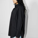 Person wearing a black oversized shirt and light blue pants against a white wall