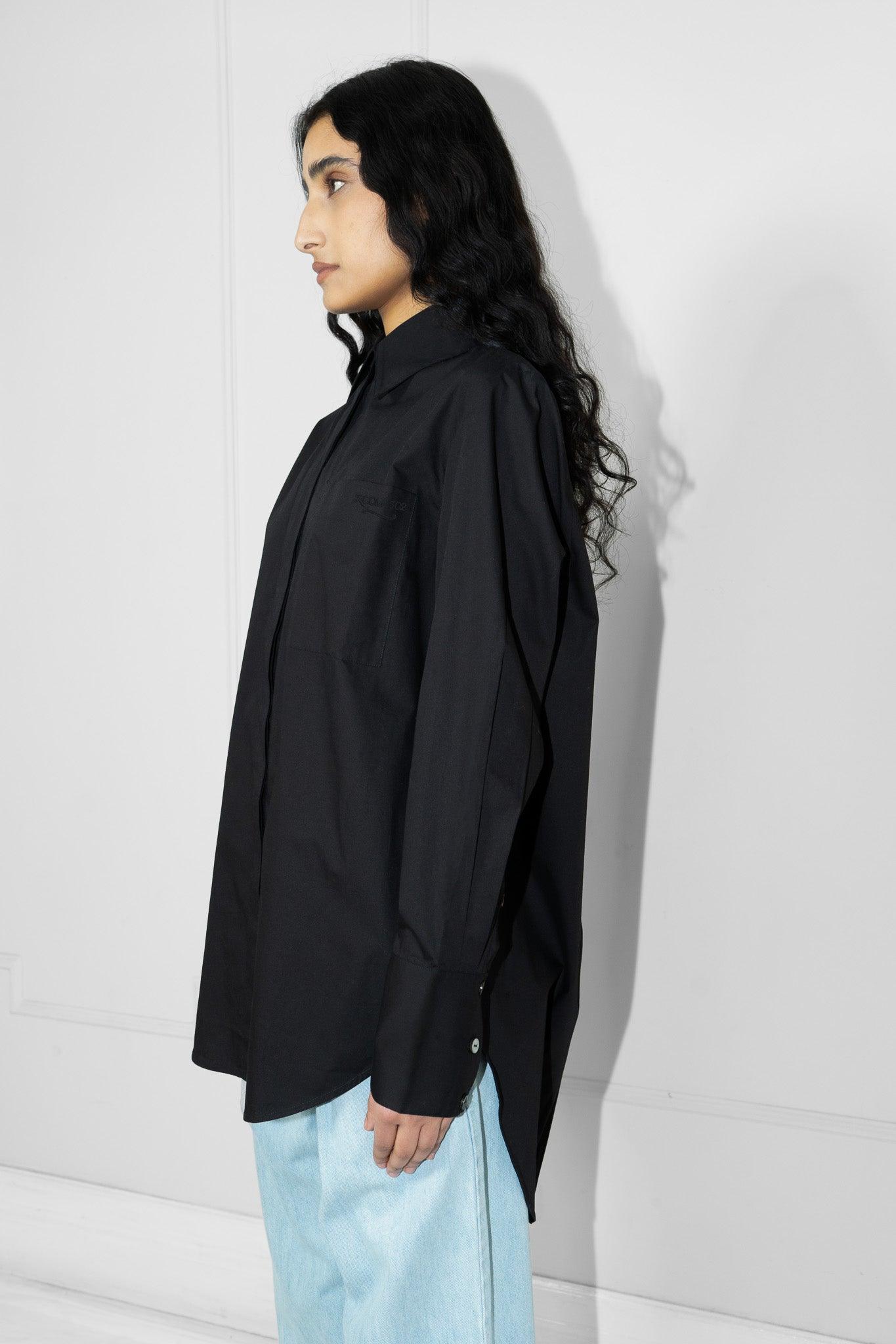 Person wearing a black oversized shirt and light blue pants against a white wall