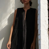 Woman wearing a black sleeveless dress against a white wall.