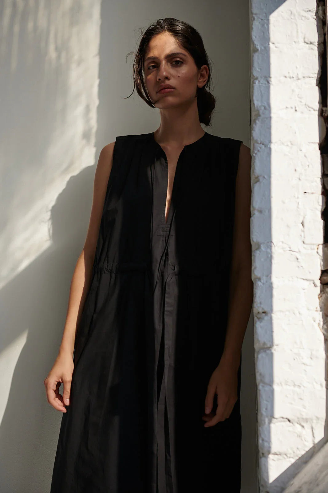 Woman wearing a black sleeveless dress against a white wall.