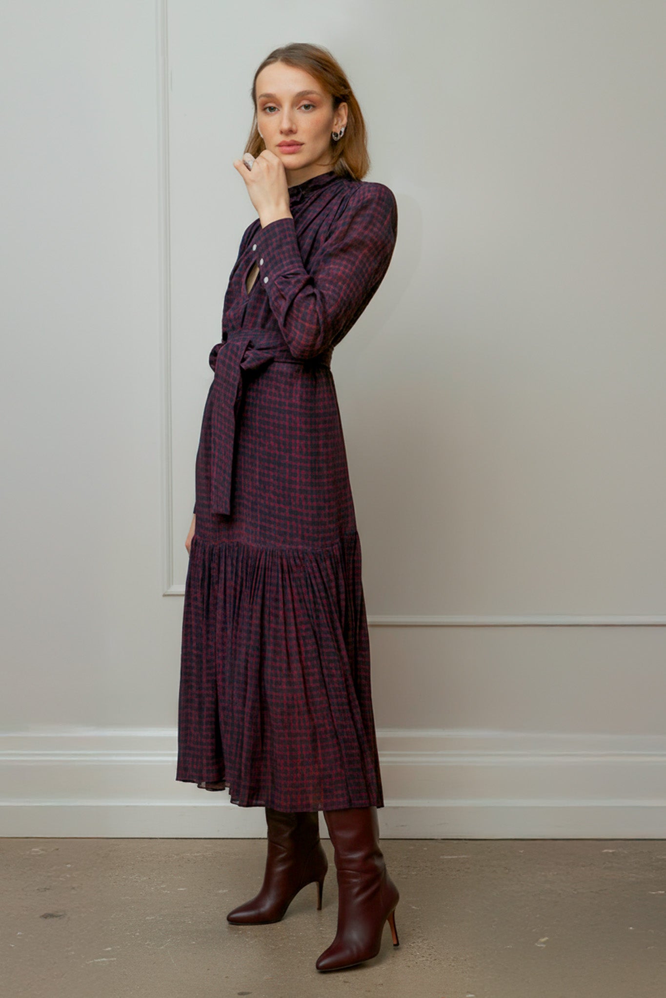 Woman wearing a dark purple print dress with a pattern, standing against a plain wall - by Room 502