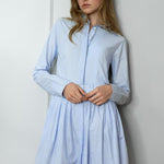 Woman wearing a light blue striped shirtdress against a white wall