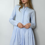 Woman wearing a light blue striped shirtdress against a white wall