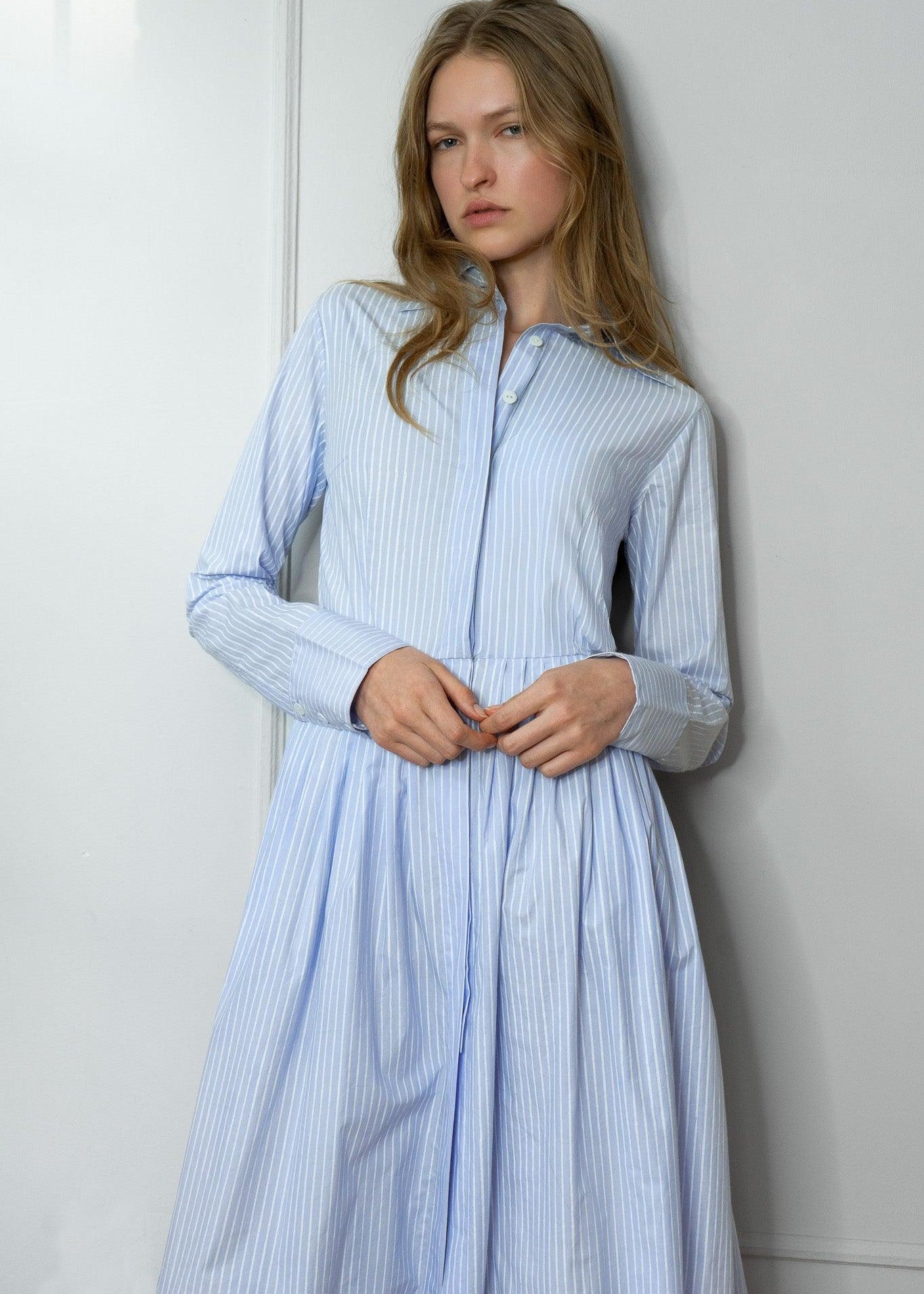 Woman wearing a light blue striped shirtdress against a white wall