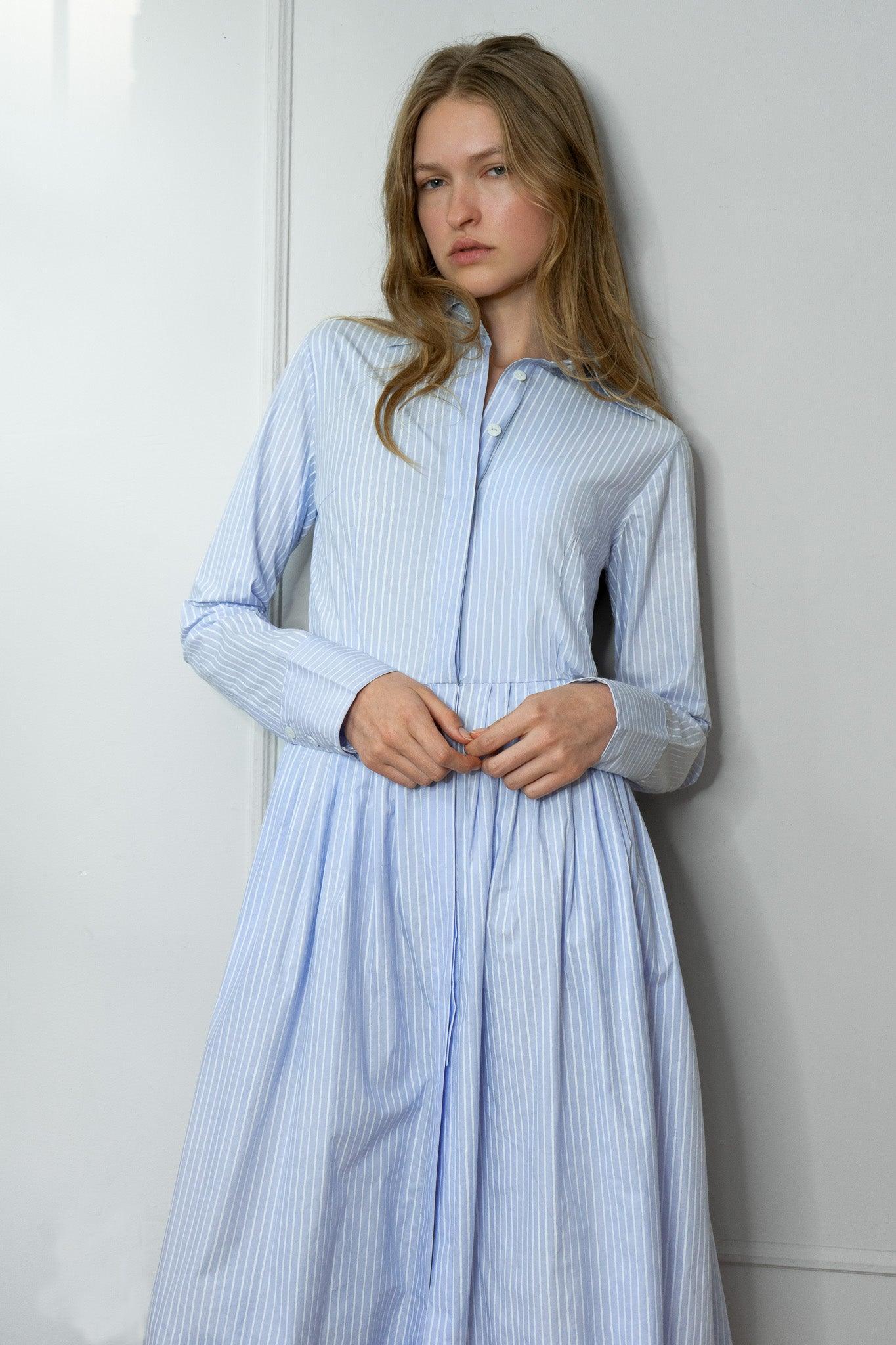 Woman wearing a light blue striped shirtdress against a white wall