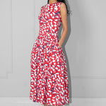 Woman wearing a red floral dress with hands in the pockets against a plain background