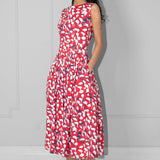 Woman wearing a red floral dress with hands in the pockets against a plain background