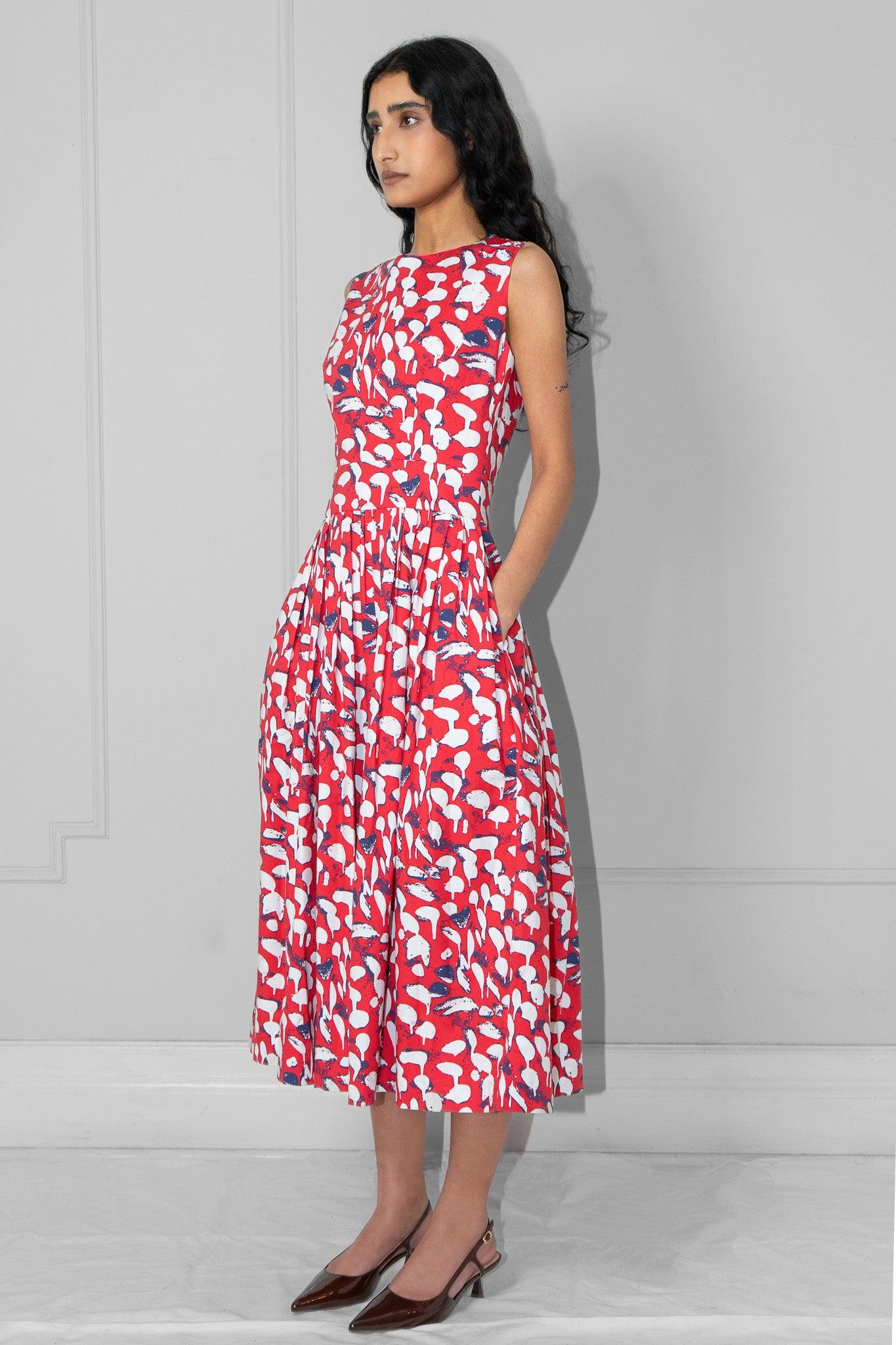 Woman wearing a red floral dress with hands in the pockets against a plain background