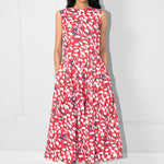 Woman wearing a red and white patterned dress with hands in the pockets against a white background