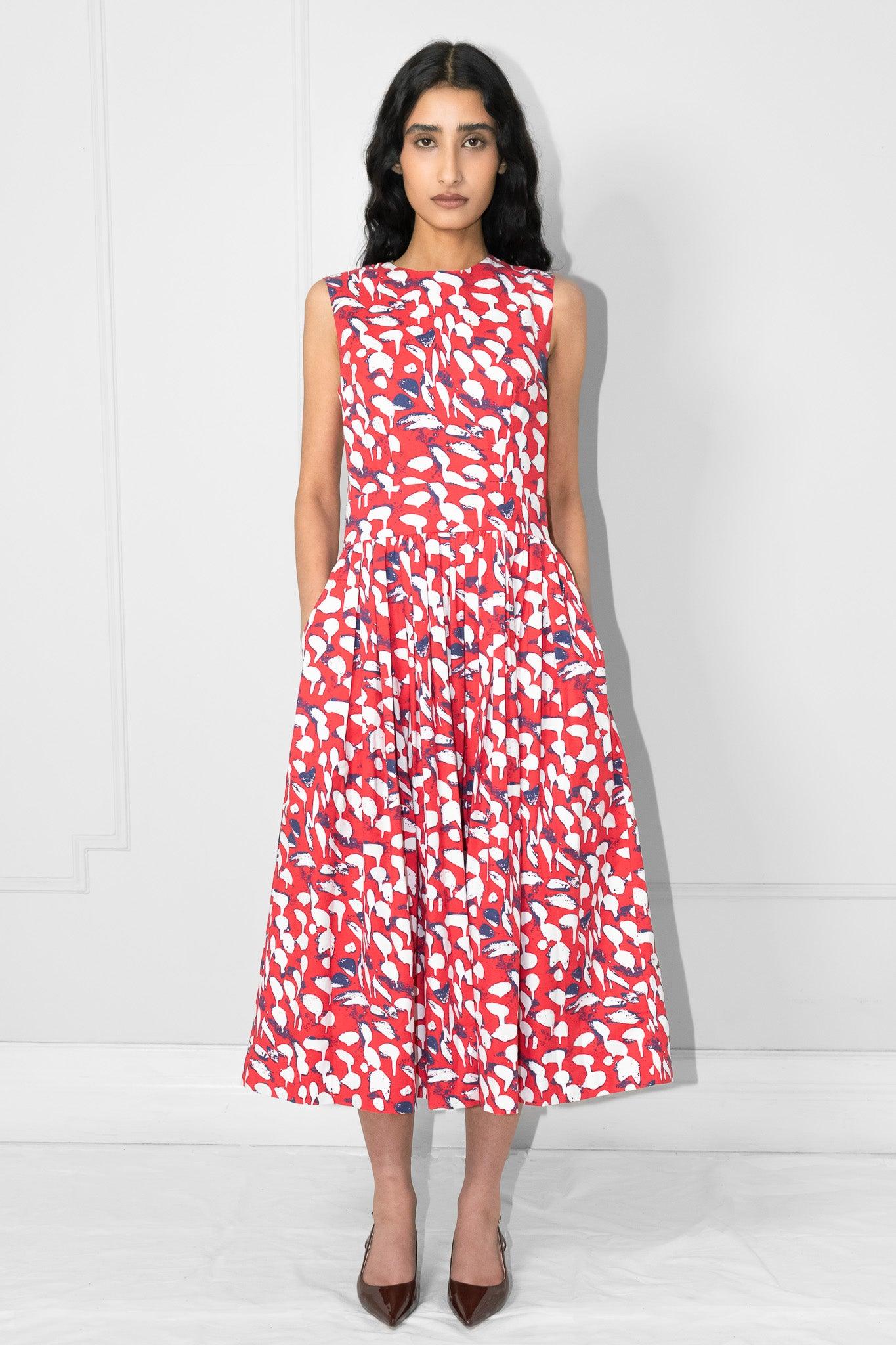 Woman wearing a red and white patterned dress with hands in the pockets against a white background