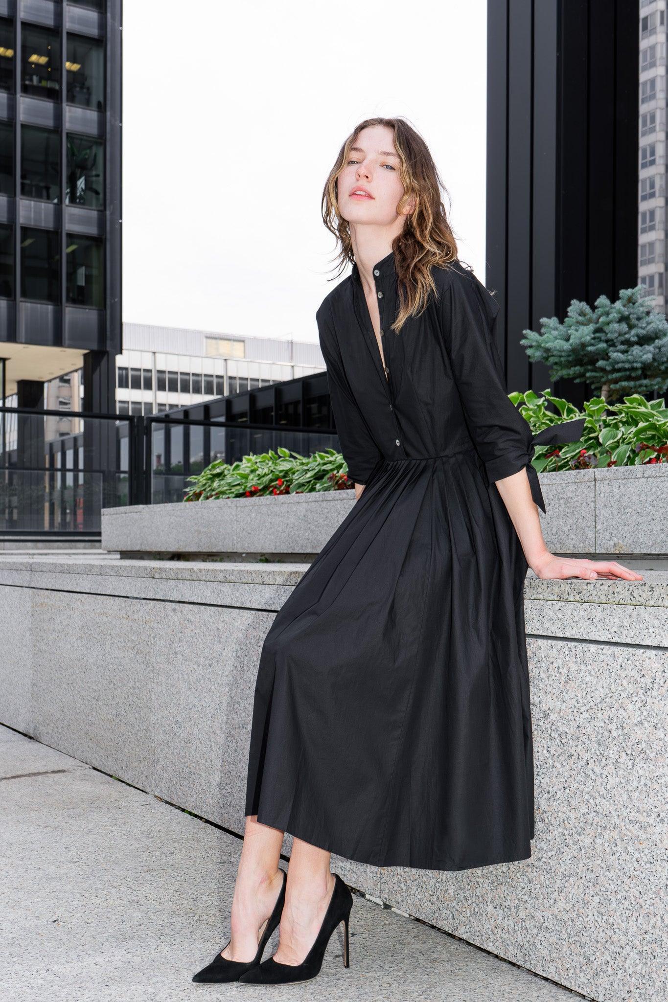 Woman in a black shirtdress standing outdoors with buildings in the background