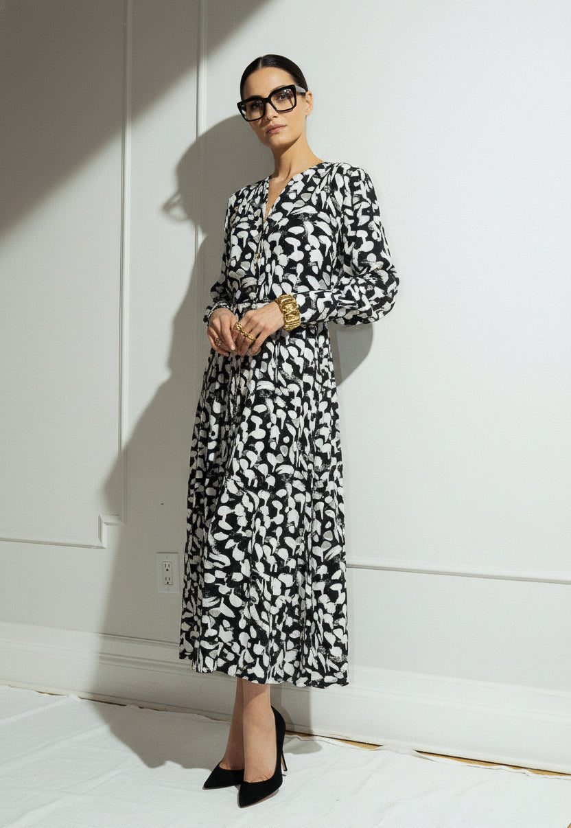 Woman wearing a black and white patterned dress against a white wall.