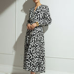 Woman wearing a black and white patterned dress against a white wall.