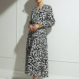 Woman wearing a black and white patterned dress against a white wall.