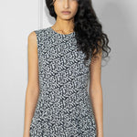 Woman wearing a sleeveless dress with a black and white pattern against a plain background