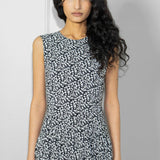 Woman wearing a sleeveless dress with a black and white pattern against a plain background