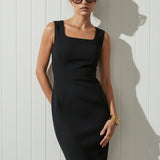 Woman wearing a black dress by Room502 and sunglasses against a white wall