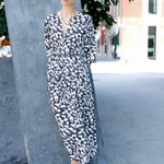 Woman in a black and white patterned dress standing outdoors on a city street.