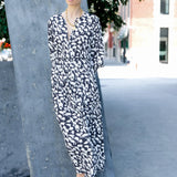 Woman in a black and white patterned dress standing outdoors on a city street.