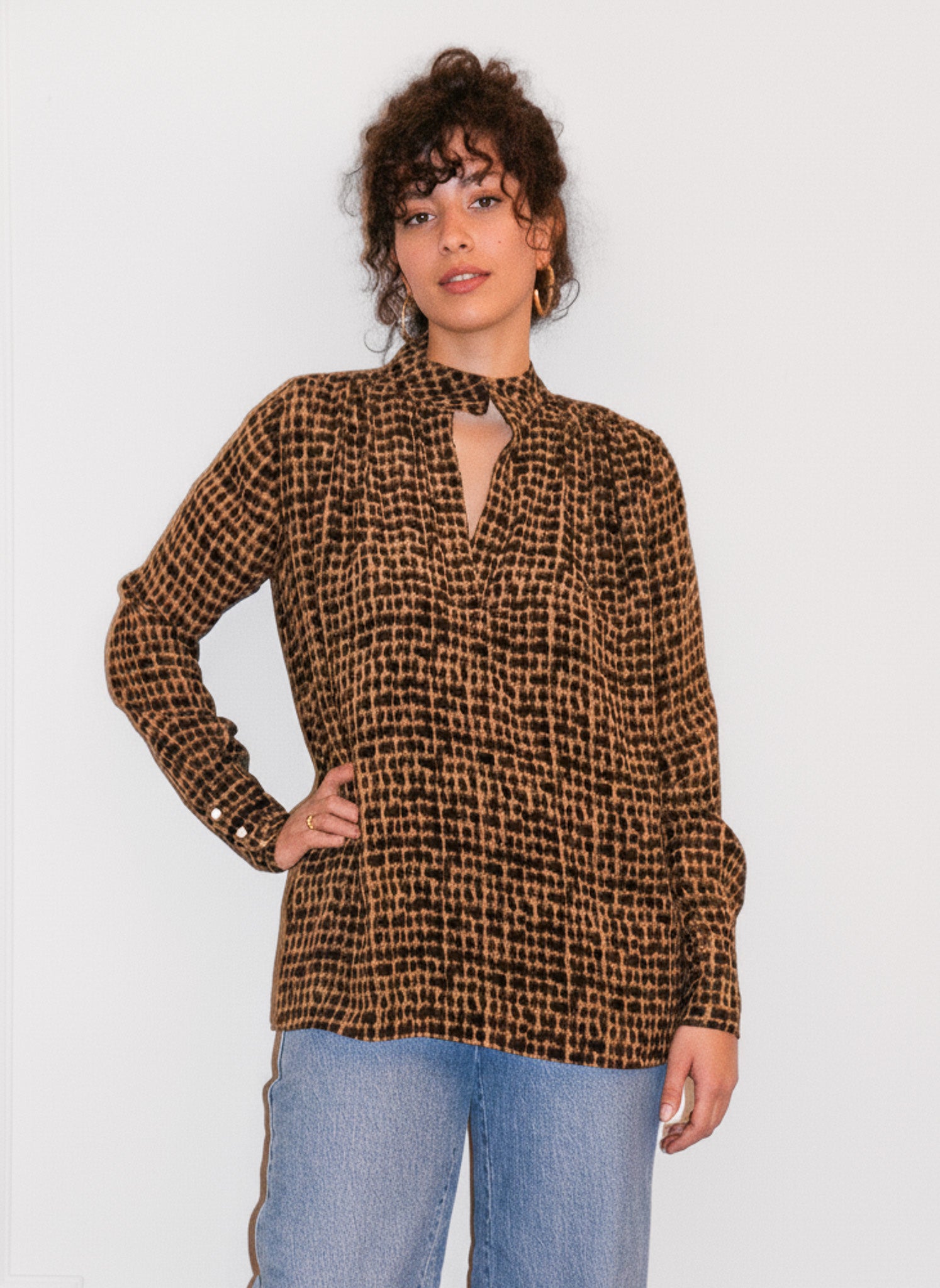 Woman wearing a brown checkered blouse and blue jeans against a white background